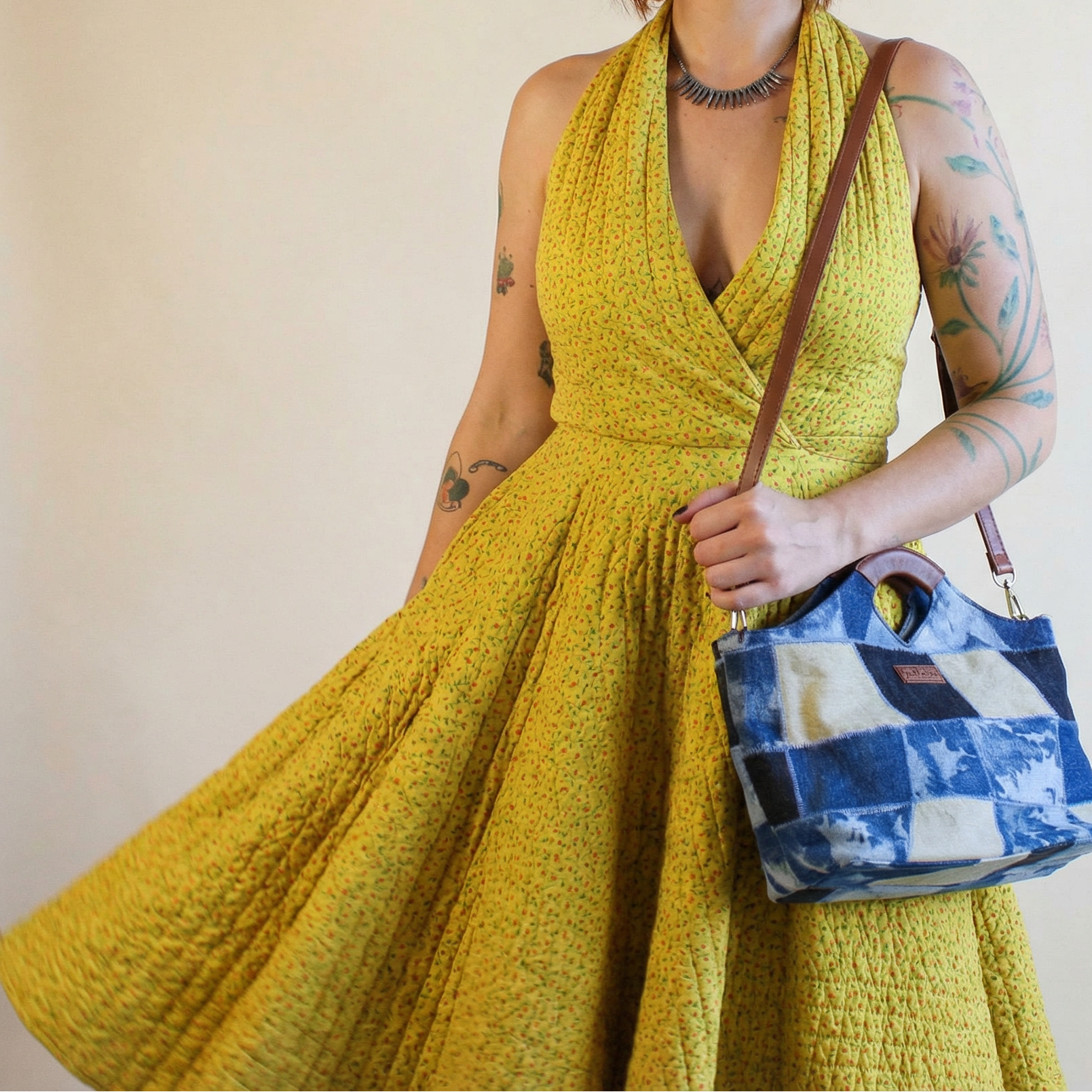 Woman in a yellow dress holding a blue and white checkered bag against a plain background